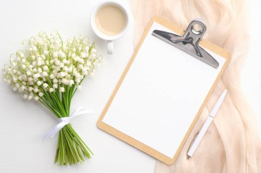 Boş pano ile zarif düz kompozisyon, bir buket çiçek zambak vadi, beyaz arka planda bir fincan kahve.