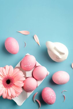 Paskalya yassı kompozisyonu pembe Paskalya yumurtaları, bahar çiçeği, turkuaz arka planda Paskalya tavşanı. Yukarıdan görünüm, düz yatış, dikey.