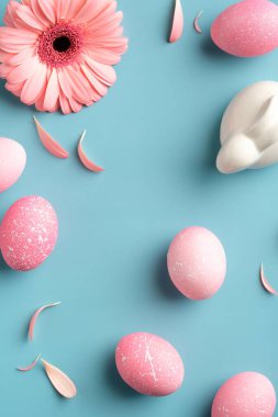 Mutlu Paskalya düzlüğü kompozisyonu. Üst manzara pembe Paskalya yumurtaları, bahar çiçekleri, turkuaz arka planda tavşan..