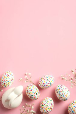 Paskalya dikey afiş modeli. Paskalya tavşanı, renkli benekli Paskalya yumurtaları, pembe arka planda bahar çiçekleri. Düz konum, üst görünüm, kopyalama alanı.