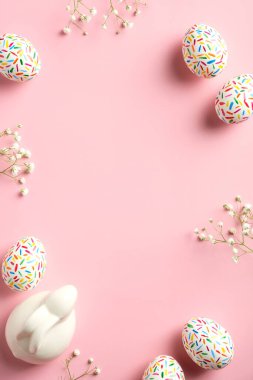 Mutlu Paskalyalar. Renkli benekli Paskalya yumurtaları, Paskalya tavşanı ve pembe arka planda bahar çiçeklerinden yapılmış çerçeve. Sosyal medya hikayeleri için dikey afiş modeli.
