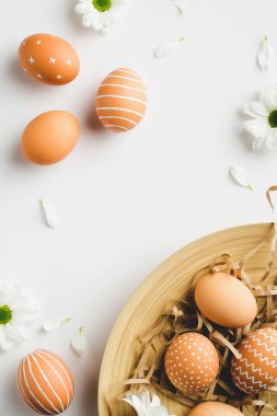 Mutlu Paskalyalar. Kuzey tarzı plaka üzerinde modern Paskalya yumurtaları, beyaz arka planda bahar çiçekleri. Şık, zarif düz konum. Üst görünüm.