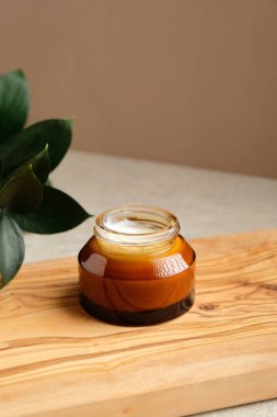 Kehribar cam kavanoz nemlendirici krem ahşap tahta üzerinde ve yeşil yaprak. Doğal organik cilt kremi, vücut losyonu, yüz kremi..