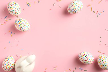 Renkli Paskalya yumurtaları, pembe arka planda tatlı ve tavşan süsleri. Paskalya kartı şablonu. Düz yatış, üst görünüm.