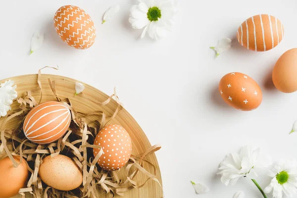 Modern Easter eggs and spring flowers on white background. Flat lay, top view, copy space. Happy Easter card design.