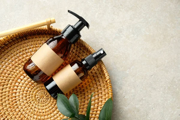 Amber glass cosmetic bottles and green leaf in rattan container on table in bathroom. Natural organic beauty products for personal hygiene, cosmetics packaging design