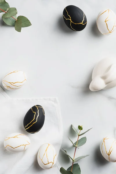 Elegant Easter flat lay composition. Luxury Easter eggs decorated gold, Easter bunny rabbit, eucalyptus on marble table. Top view.