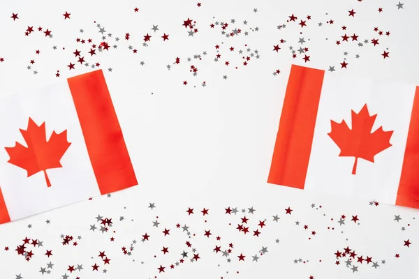 Happy Canada Day greeting card design. Canadian flags with maple leaves and confetti on white background. Flat lay, top view.