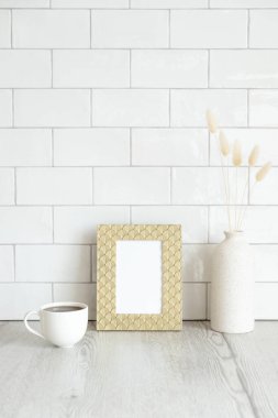 Kahvaltı hala hayattadır. Bir fincan kahve, resim çerçevesi maketi ve ahşap masada kurumuş çiçek vazosu. Arka planda tuğla kiremitler var. Hygge, İskandinav tarzı..