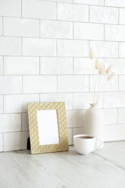 Altın fotoğraf çerçevesi maketi, kurutulmuş vazo çiçekleri, ahşap masada bir fincan kahve. Arka planda tuğla kiremitler var. Nordic, İskandinav iç mekan tasarımı. Kahvaltı hala hayattadır..