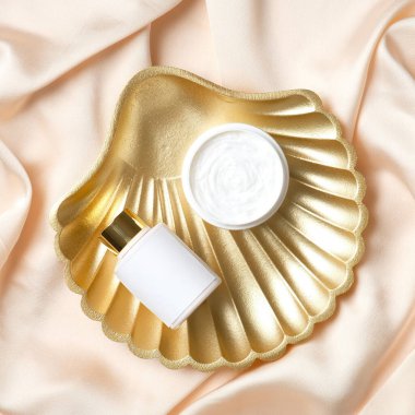 Şeftali rengi ipek üzerinde bir kavanoz nemlendirici krem ve vücut losyonu. Düz yatış, üst görünüm.