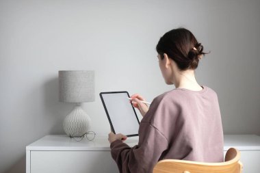 Kovid 19 tecridi sırasında tablet kullanan genç bir kadın. Basit bir İskandinav oturma odası..