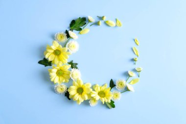 Round frame wreath with yellow flower buds and leaves on blue background. Flat lay, top view.