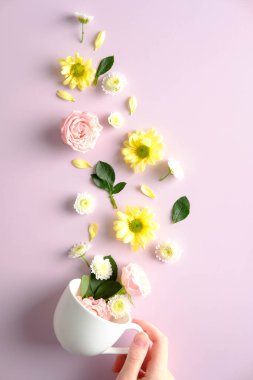Female hand holding tea cup with flowers on pnik background. Creative flat lay composition, top view.