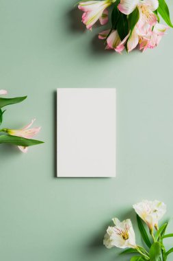 Blank paper frame card mockup and flowers on green background. Flat lay, top view, copy space. Wediing invitation, greeting card template