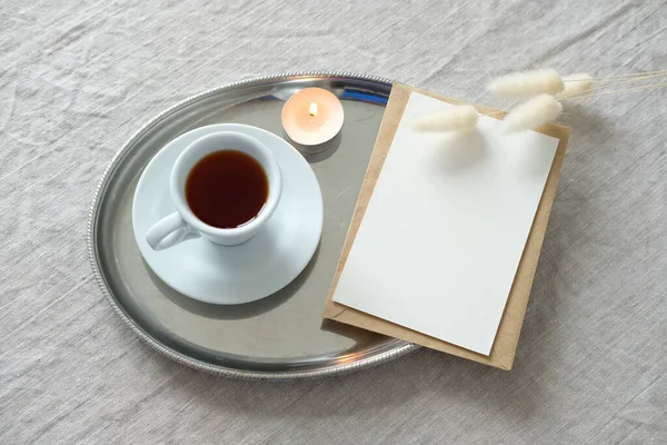 Vintage plate with blank paper card mockup, cup of coffee, candle. Flat lay, top view. Romantic breakfast concept. Wedding inviataion card template.