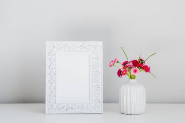 Dikey fotoğraf çerçevesi modeli ve beyaz arka planda vazoda bir buket taze çiçek. İskandinav oda dekoru. Asgari biçim.
