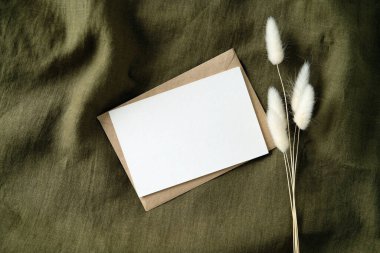 Beyaz davetiye modeli. Kurumuş çiçeklerle birlikte yeşil kumaş. Romantik mektup, düğün davetiyesi. Düz yatış, üst görünüm.