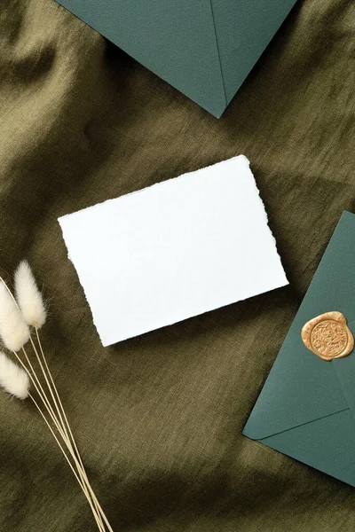 Vintage wedding stationery set top view. Rustic white invitation card, envelopes, dried flowers on green fabric. Flat lay, top view, copy space.