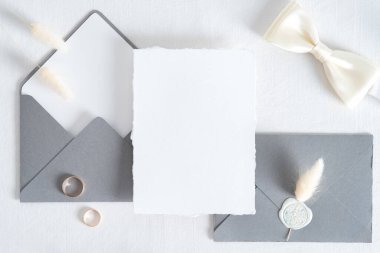 Düğün davetiyesi şablonu. Düz kâğıt kart, gri zarflar, beyaz arka planda altın yüzükler. Eski tarz. Üst görünüm.