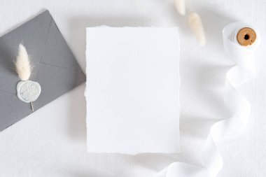 Flatlay düğün davetiyesi, mühürlü gri zarf, pastel beyaz arka planda kurumuş çiçekler. Düğün kırtasiyesi üst görünümü ayarladı.