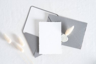 Düğün davetiyesi şablonu. Üst görünüm boş kağıt kartı, gri zarflar, beyaz arkaplanda kurumuş çiçekler..