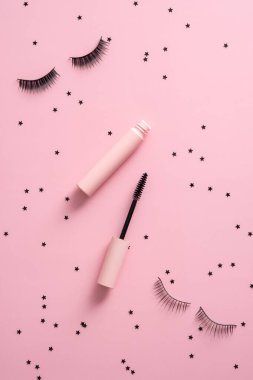Düz rimel ve takma kirpiklerle pembe arka planda konfeti vardı. Makyaj kozmetiği üst görünümü ayarladı.