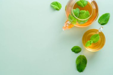 Yeşil zemin üzerinde nane çayı ve yapraklı çaydanlık. Bitki çayı konsepti. Düz konum, üst görünüm, kopyalama alanı