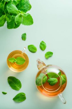 Yeşil zemin üzerinde nane yaprakları olan çay ve çaydanlık. Düz yatış, üst görünüm.