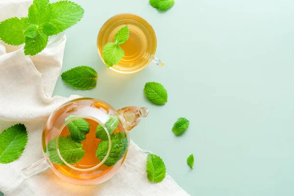 Fresh mint tea in cup and pot on green background with mint leaves. Herbal tea concept. Flat lay, top view.