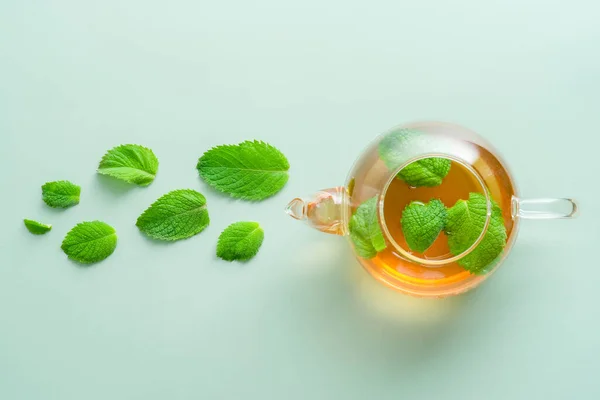 Teapot with mint tea and mint leaves on green background. Herbal tea concept. Flat lay, top view.