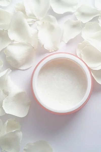 Natural face moisturizer cream with rose petals on white background. Flat lay, top view.