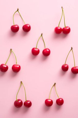 Pembe arka planda olgun kırmızı kirazlar. Düz yatış, üst görünüm.