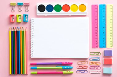 Okul kırtasiye seti pembe arkaplan manzaralı. Renkli ofis malzemeleri ve boş kağıt not defteri, okula dönüş konsepti..