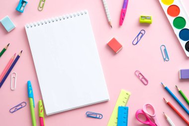 Renkli okul malzemeleri ve pembe arka planda kağıt not defteri. Okul konseptine geri dönelim. Düz yatıyordu, üstten, yukarıdan..