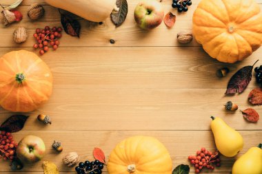 Balkabaklarından, düşen yapraklardan, elmalardan, kırmızı meyvelerden, cevizlerden, ahşap masadaki çam kozalaklarından oluşan sonbahar çerçevesi. Şükran Günü, Cadılar Bayramı, Sonbahar Hasat konsepti. Düz konum, üst görünüm, kopyalama alanı.