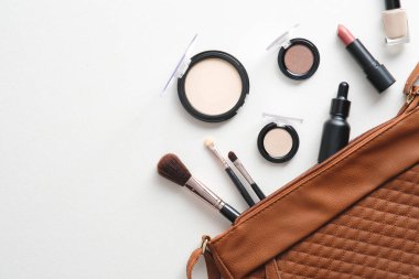 Profesyonel makyaj malzemelerinin olduğu düz bir çanta ve kahverengi arka planda aletler vardı. Kopyalama alanı olan üst görünüm.