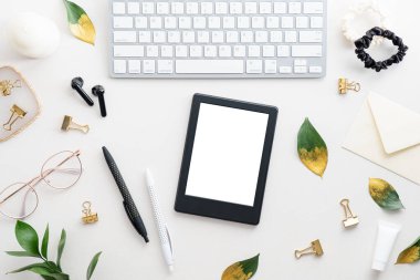 Kitap tableti, klavye, kalem, gözlük, kulaklık ve beyaz arka planda düşme yaprakları olan düz bir ofis masası. Kadınsı çalışma alanı üst görünümü.