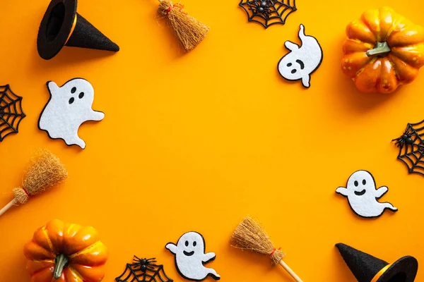 Happy Halloween holiday concept. Halloween decorations, pumpkins, ghosts, witches hats, brooms on orange background. Halloween party greeting card mockup with copy space. Flat lay, top view.