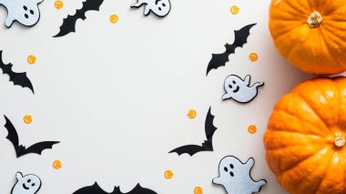 Cadılar Bayramı arkaplanı, beyaz masa üzerinde sevimli süslemeler ve balkabakları. Düz konum, üst görünüm, kopyalama alanı. Cadılar Bayramı partisi davetiye maketi.