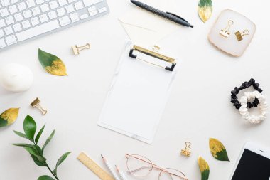 Kağıt pano, bilgisayar klavyesi, bitki, beyaz masa üzerinde kadın aksesuarları olan üst görünüm çalışma alanı. Merkez ofis masası..