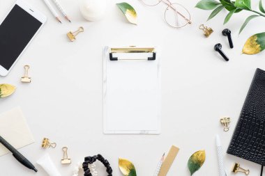 Beyaz arkaplanda pano, telefon, defter, aksesuarlar olan ofis masası çalışma alanı.