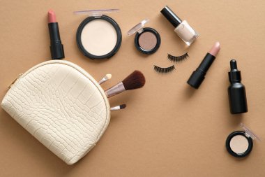 Kahverengi masaya dökülen kozmetik ürünlerle dolu makyaj çantası. Makyaj çantasının içinde güzellik ürünleri var. Düz yatış, üst görünüm