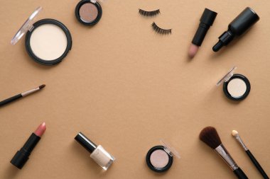 Kahverengi arka planda makyajlı profesyonel kozmetikten yapılmış çerçeve. Düz yatış, üst görünüm.