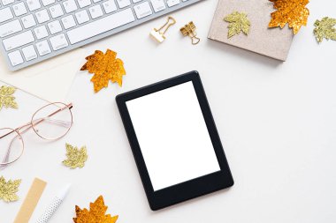 Beyaz masadaki boş ekran, klavye, gözlük, defter ve akçaağaç yapraklarıyla dijital tablet modeli. Güz blogcusu çalışma alanı. Düz yatış, üst görünüm.