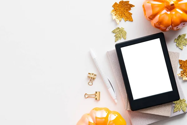 Autumn background with digital tablet ebook mockup, pumpkins, maple leaves on white table. Flat lay, top view.