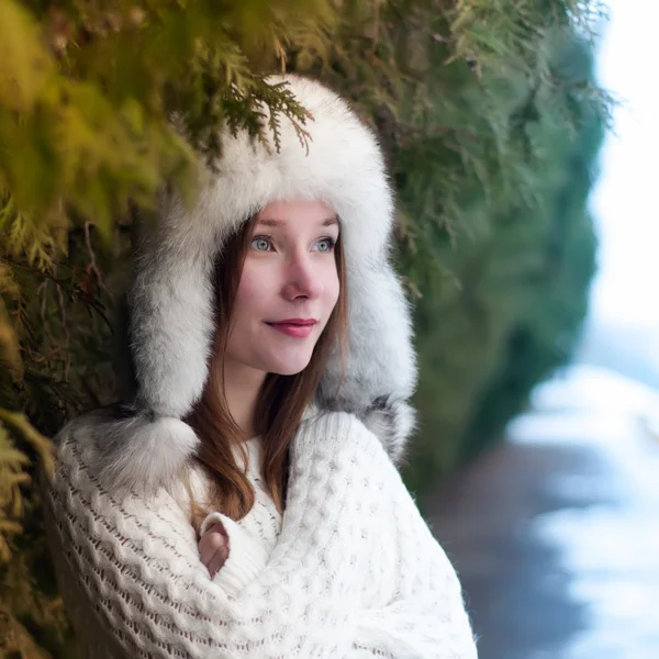 Retrato de uma jovem menina bonita em um boné com abas de ouvido em um parque de inverno fresco — Fotografia de Stock