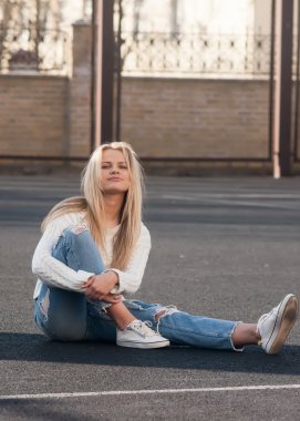 Oldukça şık sarışın genç kadın yırtık kot ve beyaz Kazak giymiş