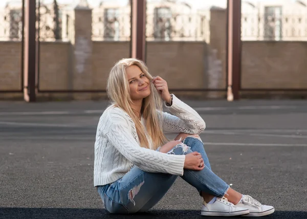 Junge hübsche blonde Frau in zerrissenen Jeans und weißem Pullover — Stockfoto