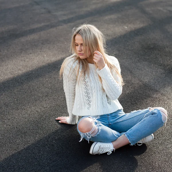 Young pretty fashionable blonde woman dressed in ripped jeans and white sweater — Stock Photo, Image